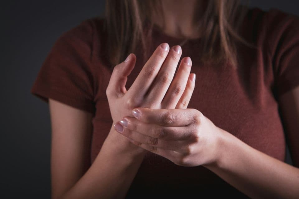 A woman holds her painful hand and wrist, a common early sign of arthritis